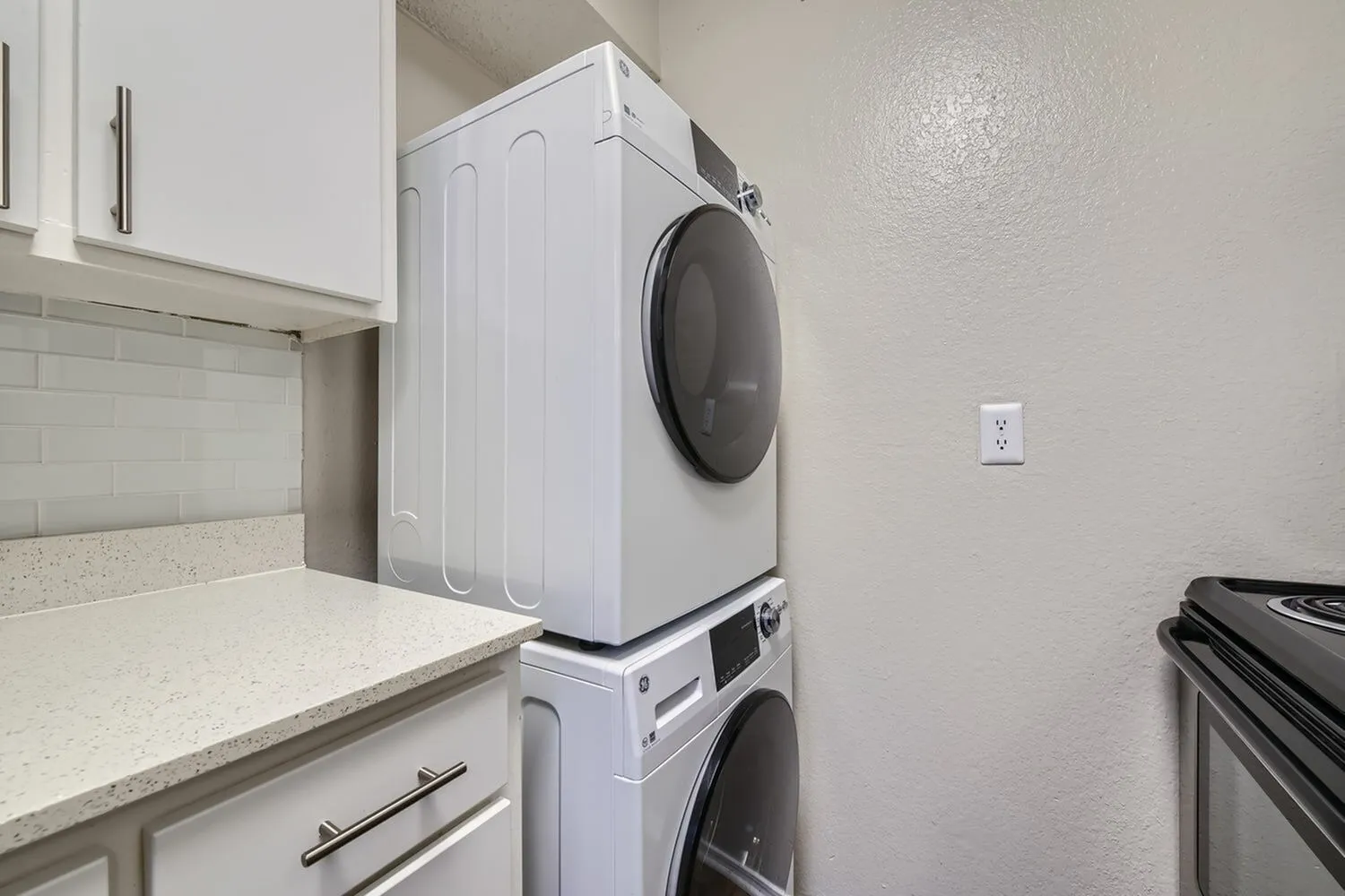 Laundry room, stacked white washer and dryer, quartz countertops, white cabinetry, subway tile backsplash