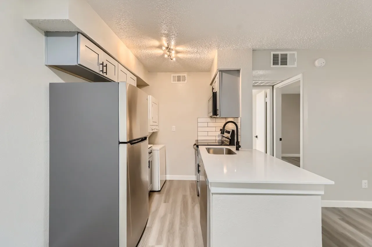 Kitchen with white quartz countertops, stainless appliances, white shaker cabinetry, wood-style plank flooring