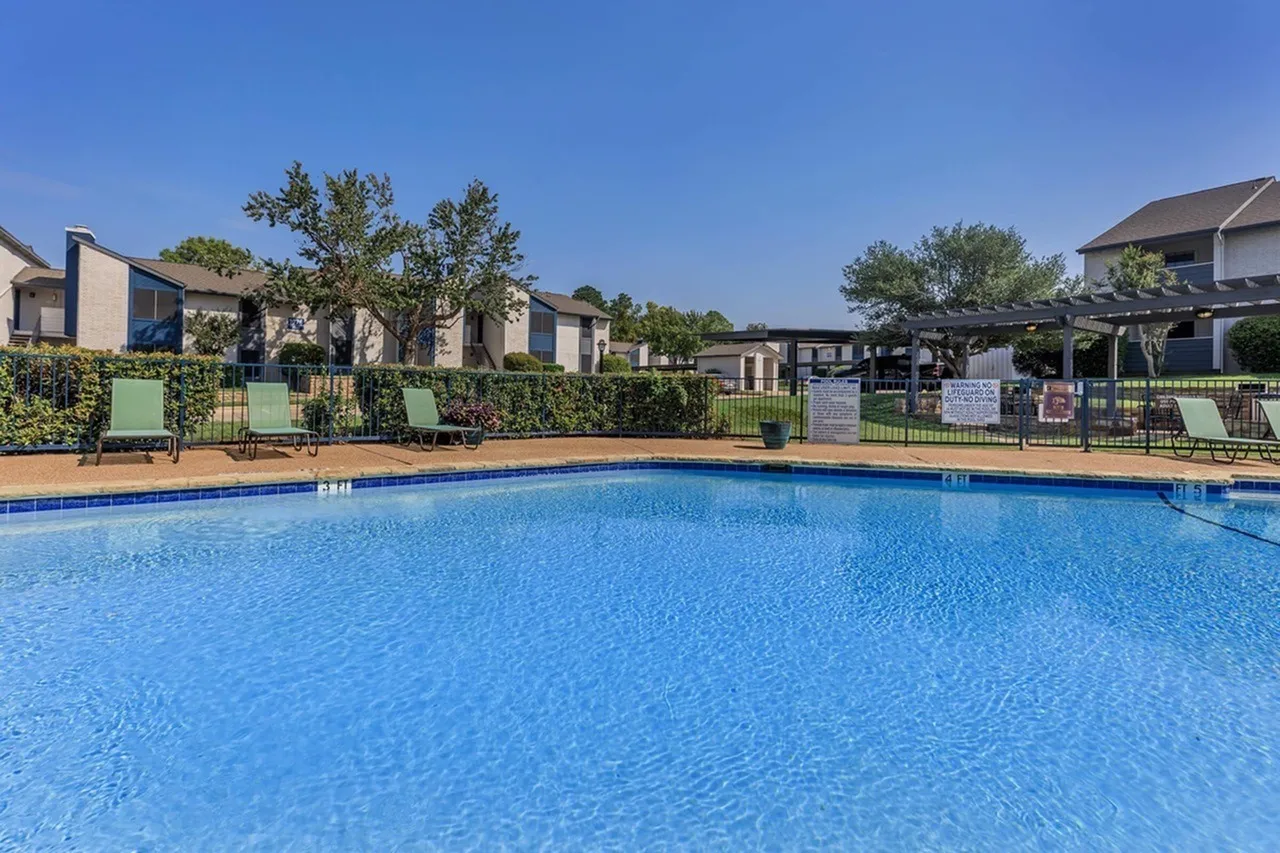 Resort-style swimming pool, lounge seating, green fencing, residential buildings, clear blue sky