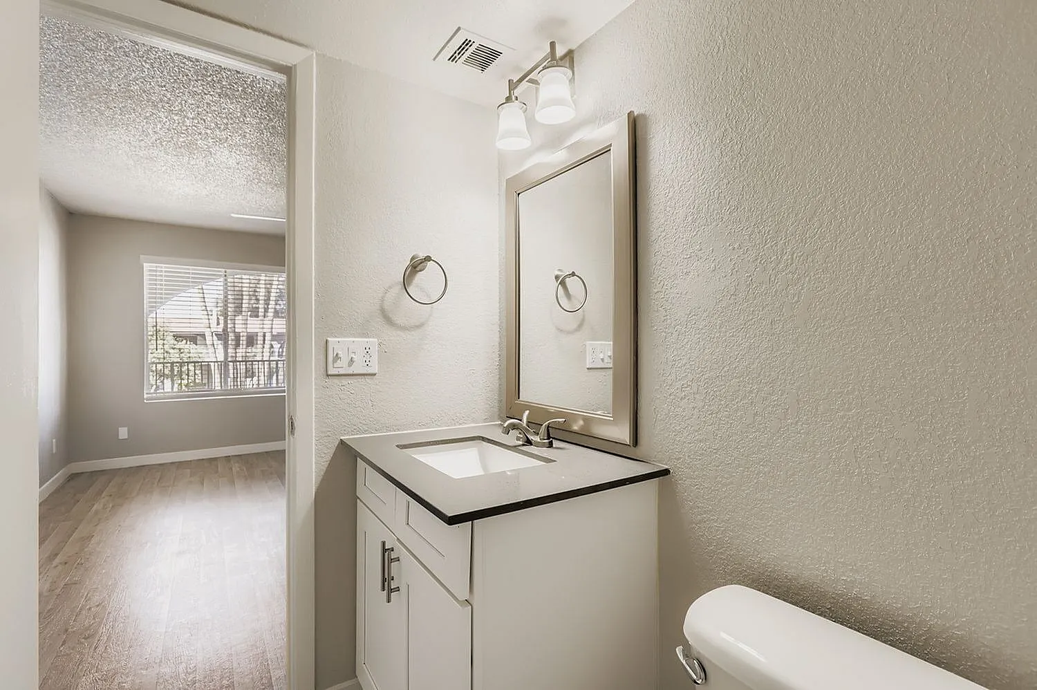 Bathroom, white vanity, white ceramic sink, framed mirror, wood-style plank flooring