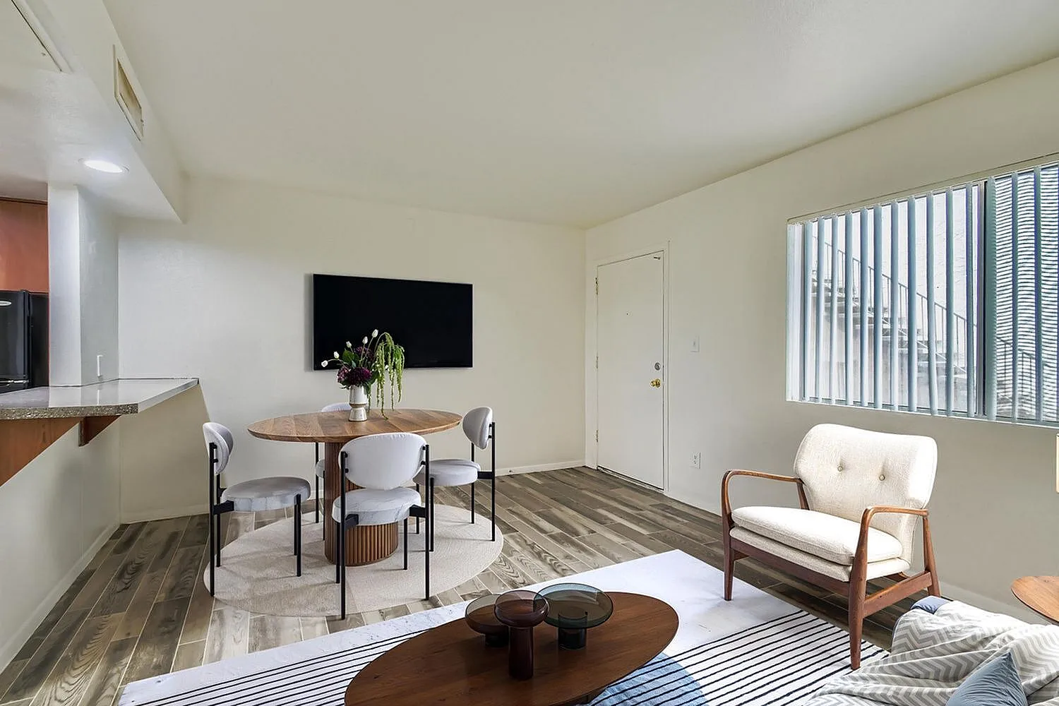 Living room with wood-style plank flooring, round dining table with chairs, flat-screen TV, white accent chair