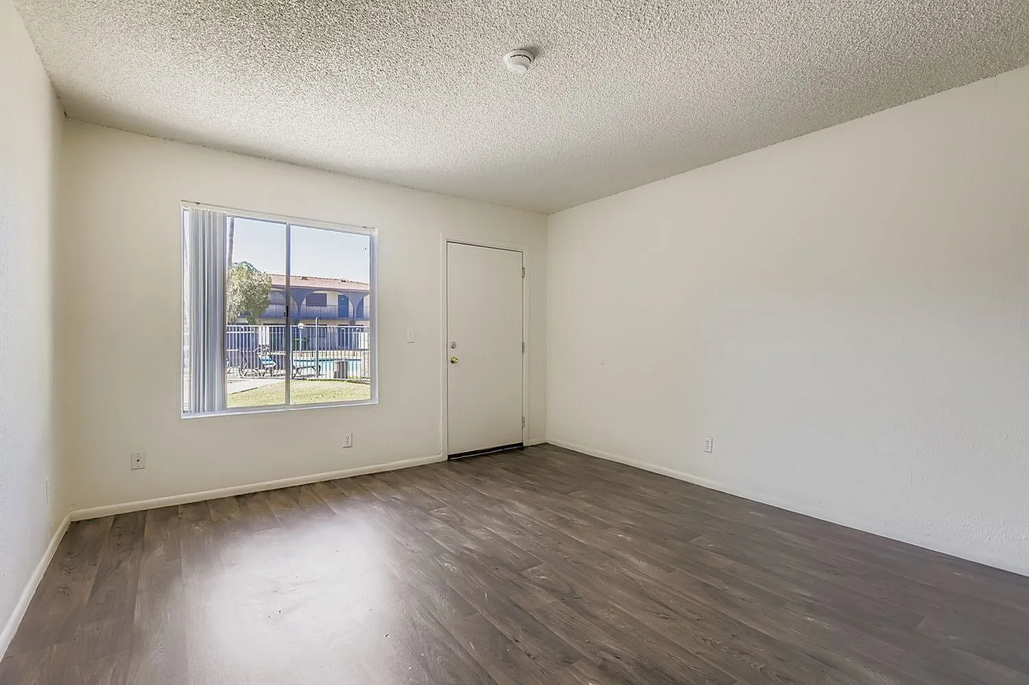 Bedroom, wood-style plank flooring, large window with blinds, entry door, textured ceiling
