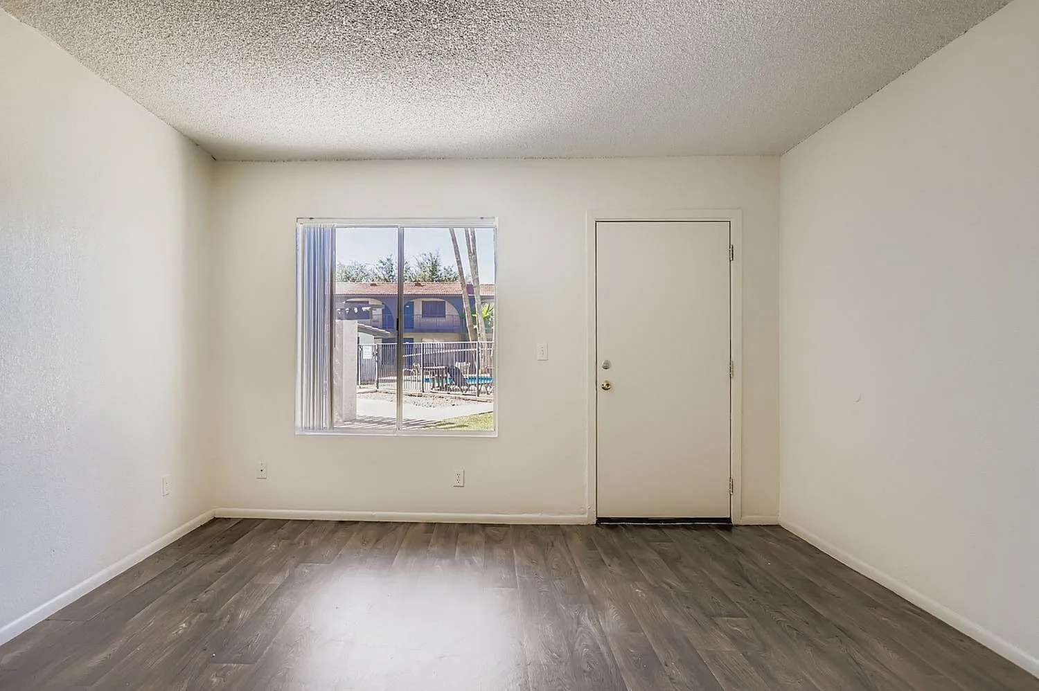 Bedroom, wood-style plank flooring, textured ceiling, window with vertical blinds, entry door