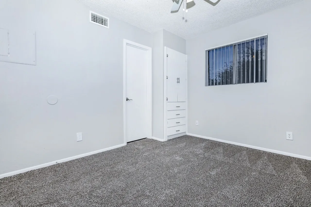 Bedroom, gray carpeting, white closet doors, built-in dresser, window with blue blinds