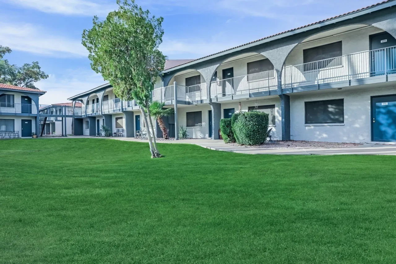 Residential courtyard, manicured lawn, white multi-story buildings with blue accents, arched balconies