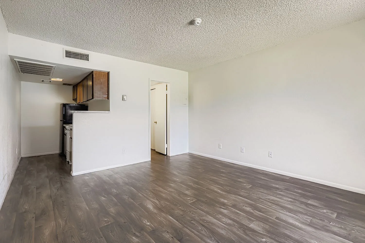 Living room and kitchen, wood-style plank flooring, white walls, stainless appliances