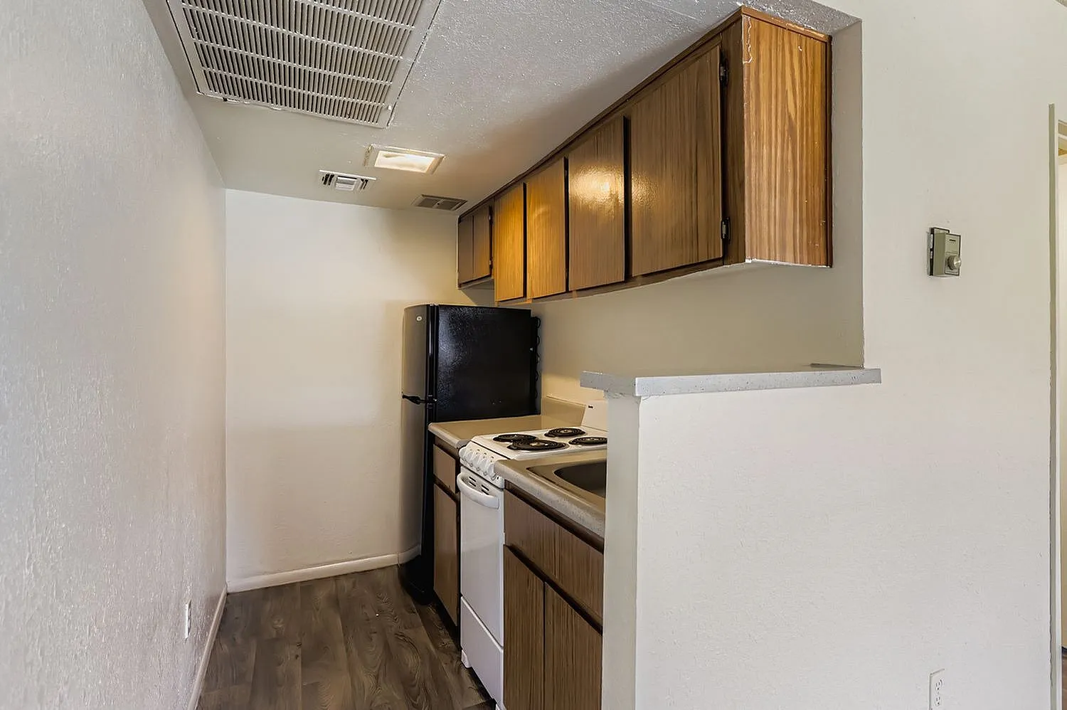 Galley kitchen, wood-style cabinetry, white electric stove, black refrigerator, wood-style plank flooring