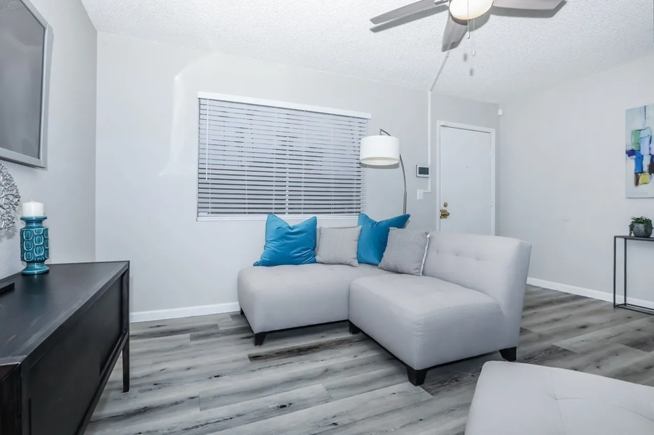Living room, white sectional sofa, blue accent pillows, wood-style plank flooring, ceiling fan