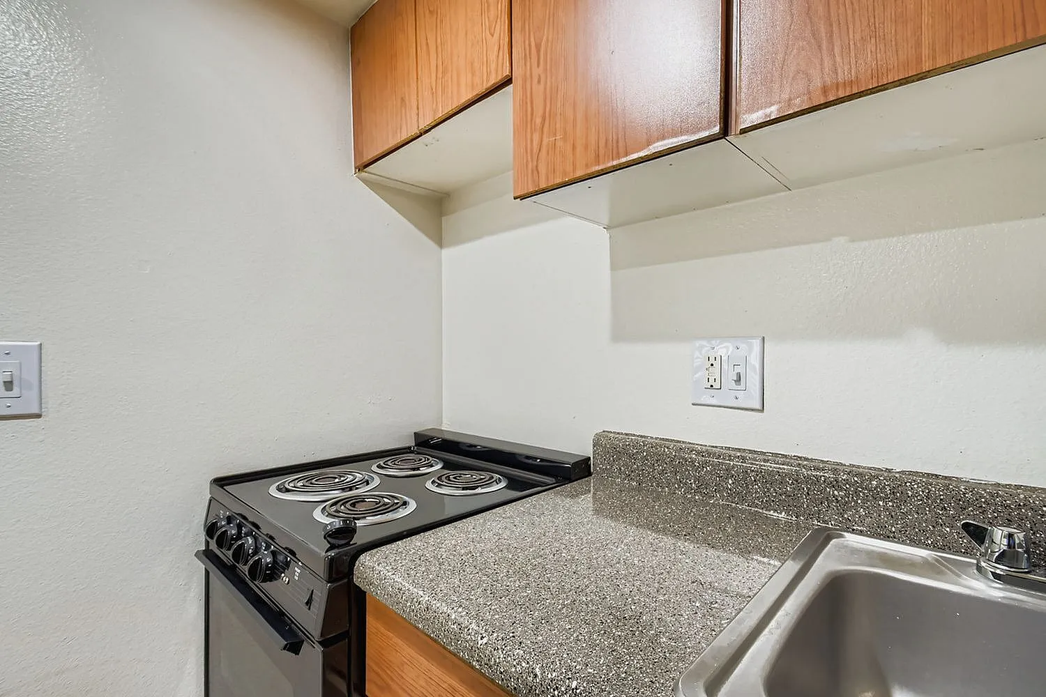 Kitchen, black cooktop, speckled gray countertops, wood cabinetry, stainless sink