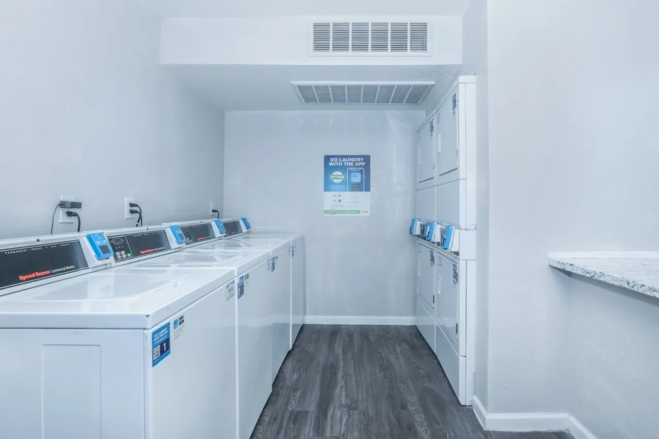 Laundry room, multiple white front-load washers, blue detergent dispensers, wood-style plank flooring