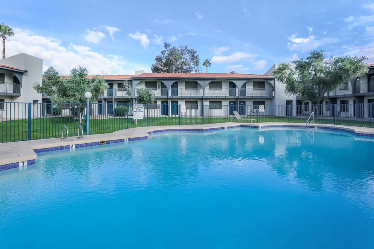Swimming pool, lounge chairs, white metal fencing, multiunit residential buildings