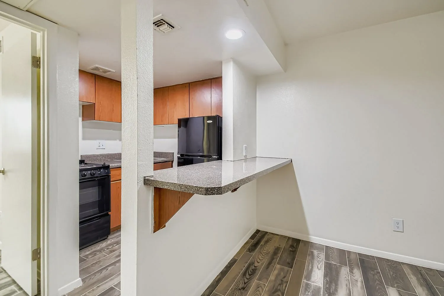 Kitchen with orange cabinetry, granite countertops, breakfast bar, wood-style plank flooring, stainless appliances