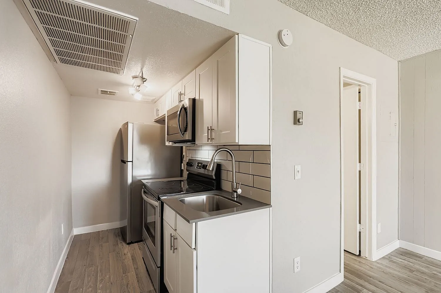 Kitchen, white shaker cabinetry, stainless steel appliances, gray subway tile backsplash, wood-style plank flooring