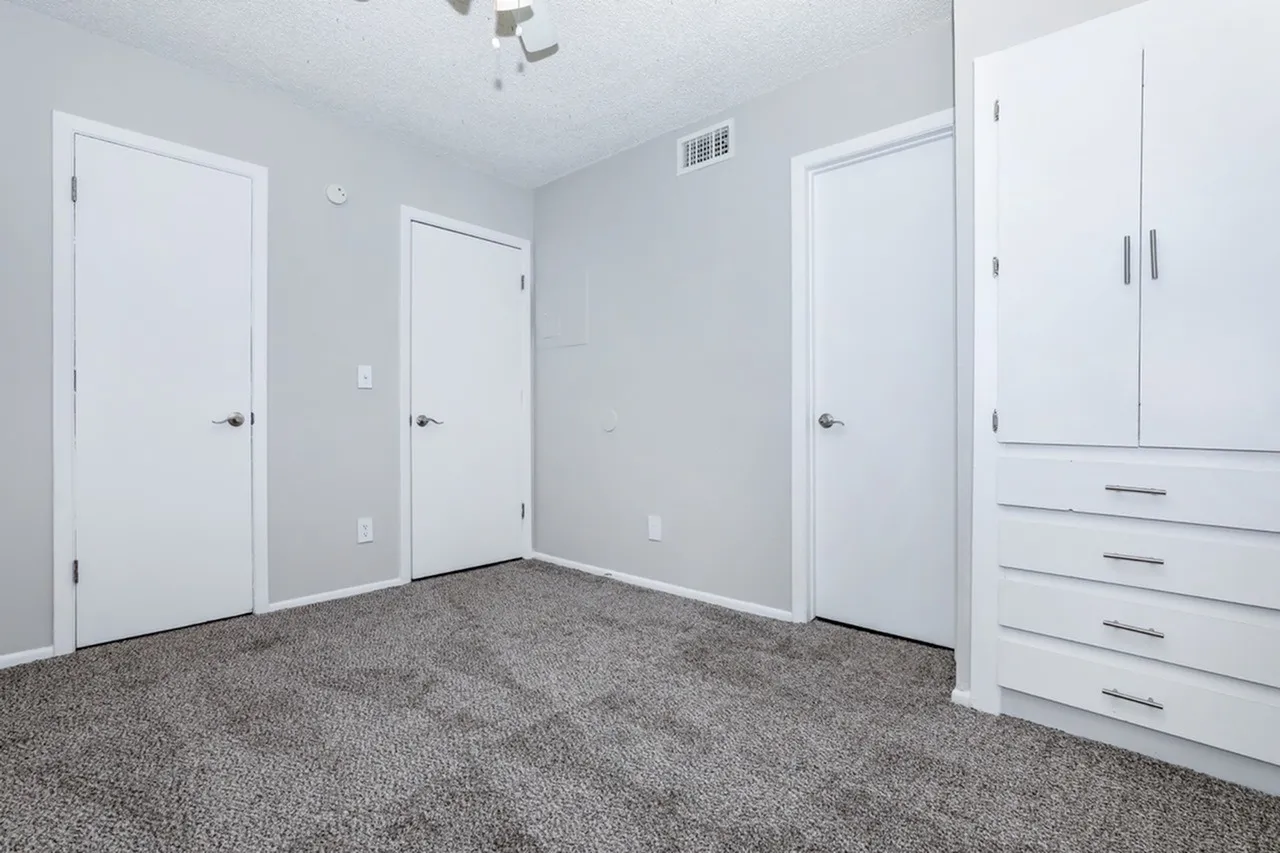 Primary bedroom, gray carpet flooring, white closet doors, built-in wardrobe
