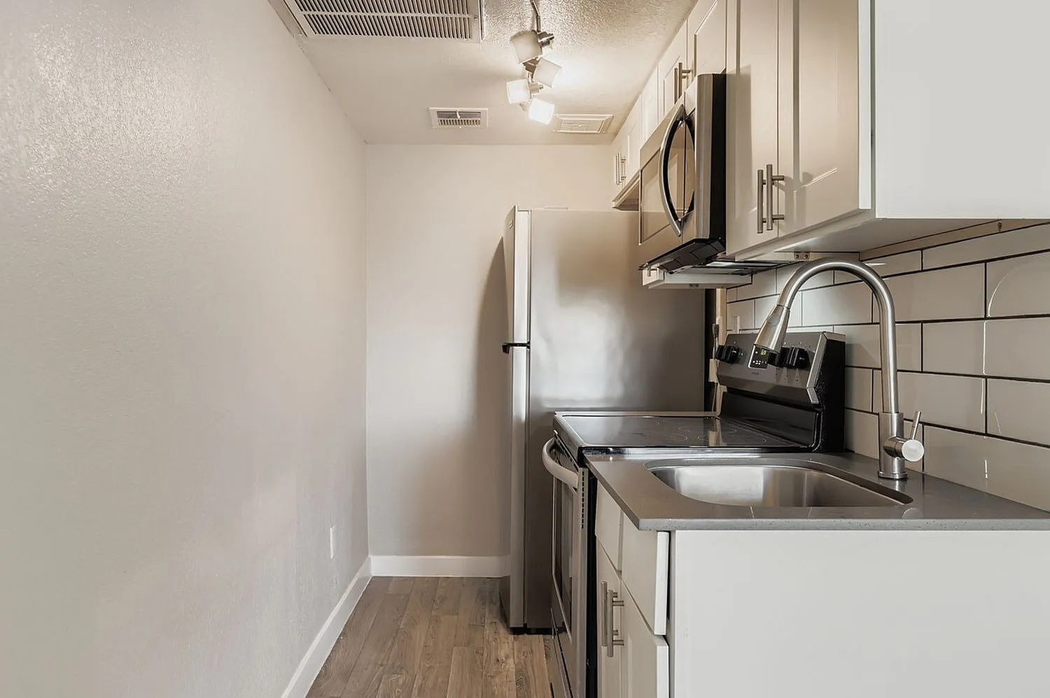 Kitchen, white shaker cabinetry, stainless steel appliances, subway tile backsplash, wood-style plank flooring