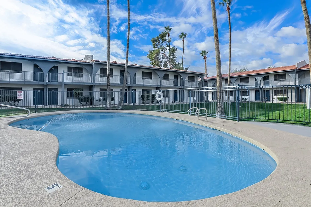 Community pool, curved blue water, palm trees, metal railings, multi-story residential buildings