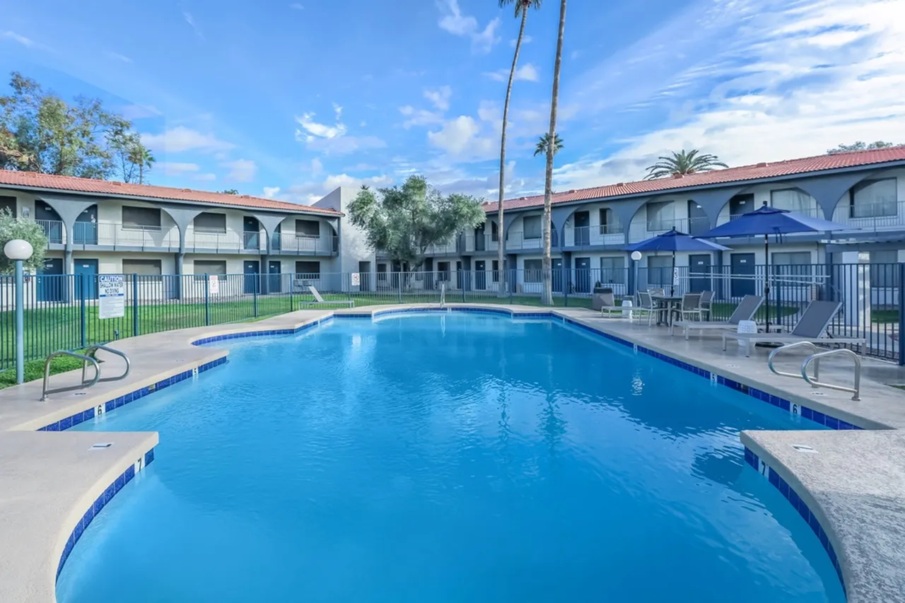 Resort-style swimming pool, blue water, concrete decking, lounge seating, blue umbrella
