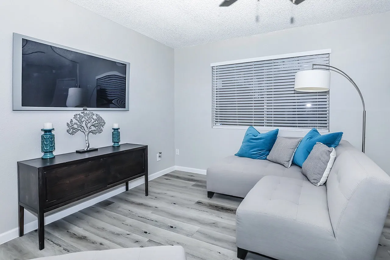 Bedroom, white upholstered bed, blue accent pillows, wood-style plank flooring, black dresser, arc floor lamp