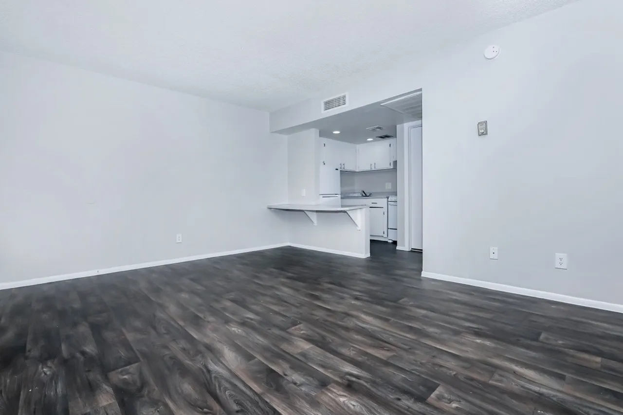 Studio apartment, wood-style plank flooring, white walls, kitchenette with appliances