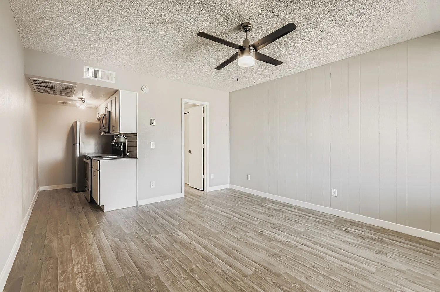 Living room and kitchen, wood-style plank flooring, ceiling fan, white cabinetry, stainless appliances