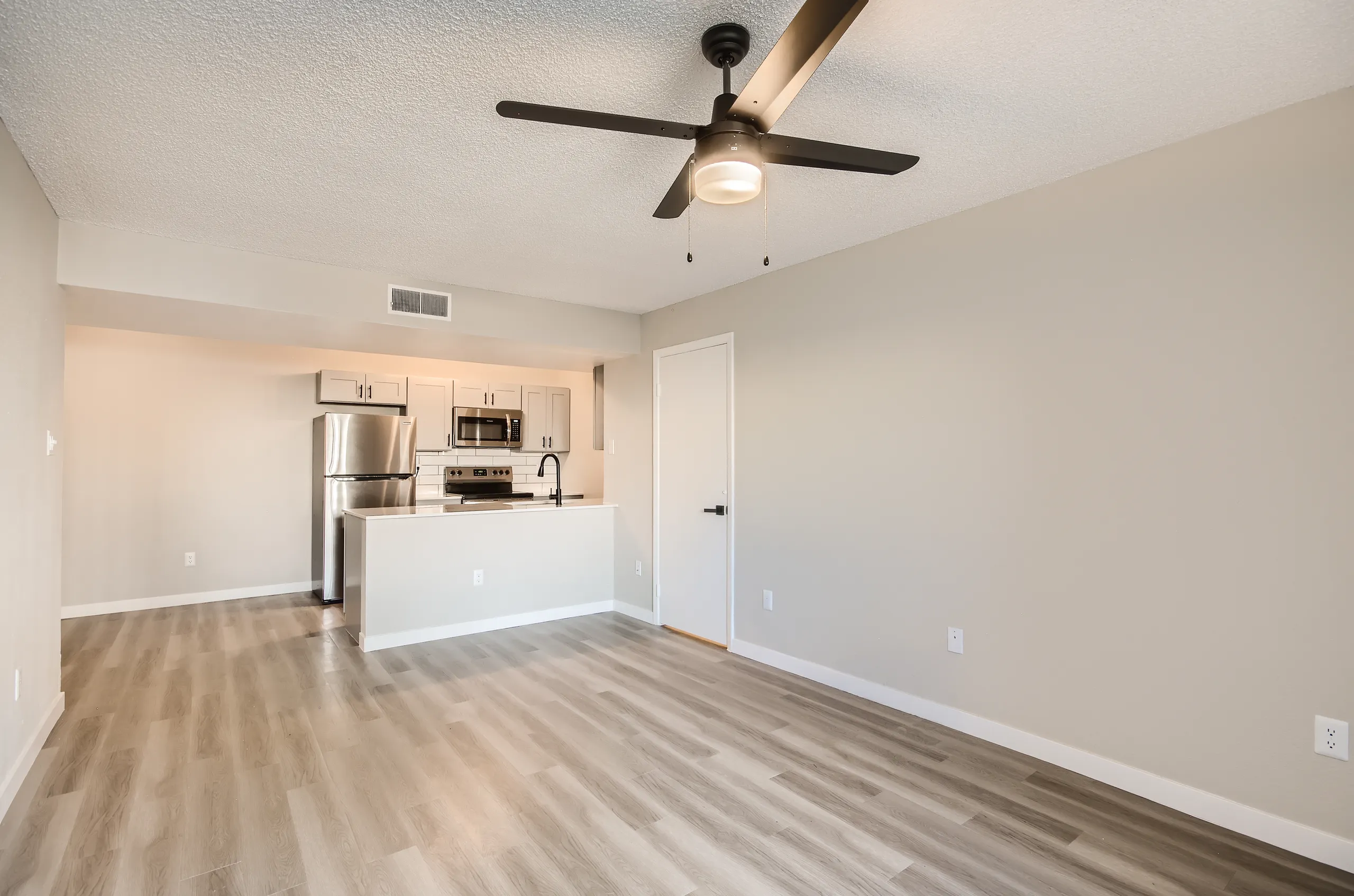 Open living room, ceiling fan, kitchen view, wood-style plank flooring