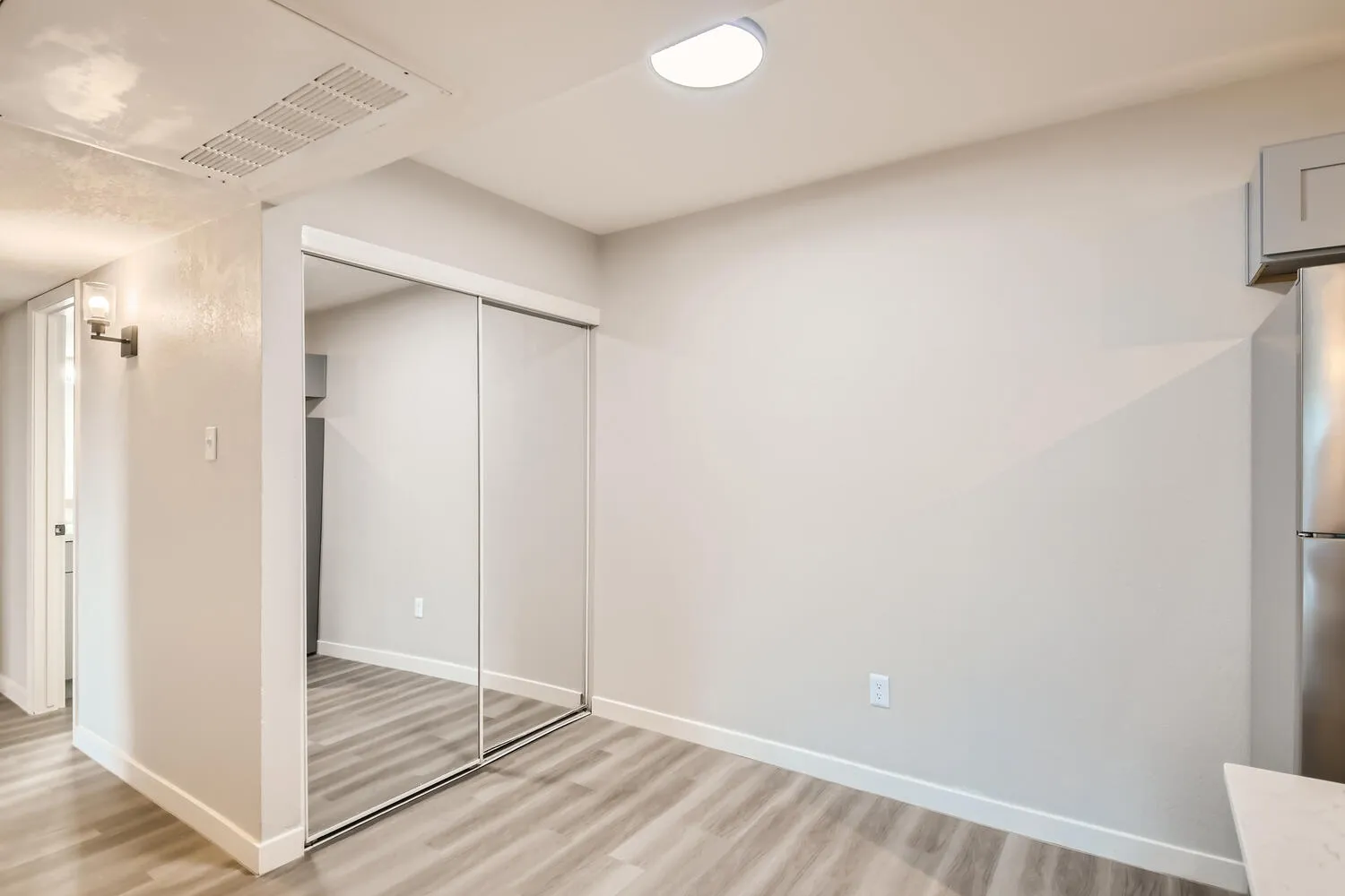 Bedroom, mirrored closet doors, wall sconce lighting, wood-style plank flooring