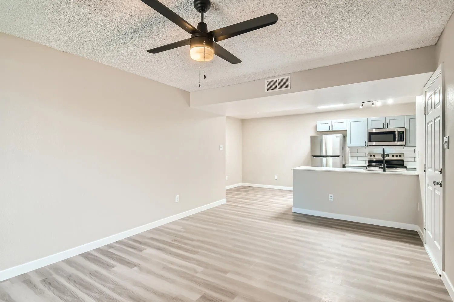 Open living room, ceiling fan, kitchen view, wood-style plank flooring