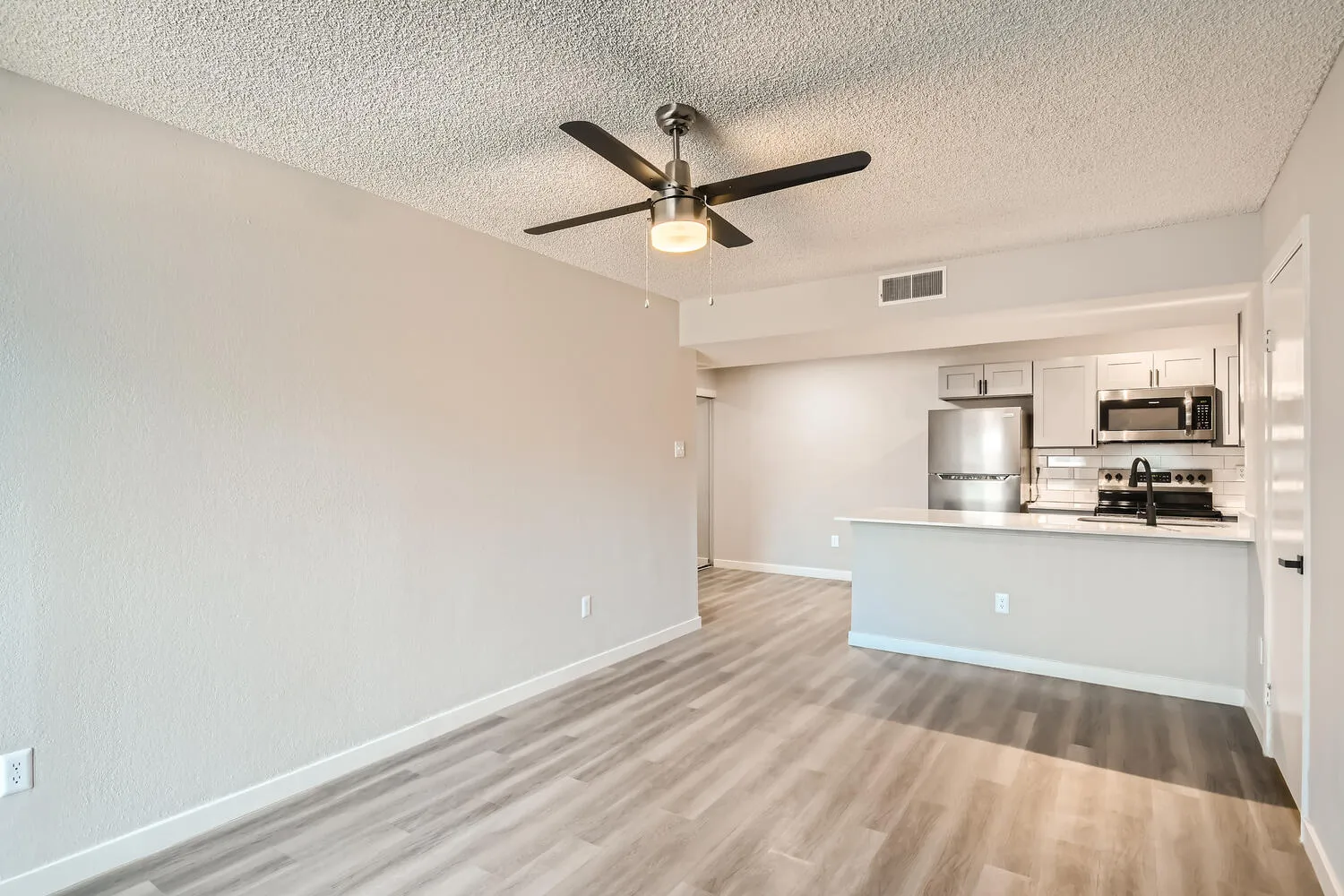 B2 Platinum living room, wood-style plank flooring, ceiling fan, open kitchen view