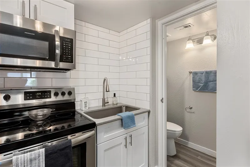 Stove and sink area, subway tile, view into bathroom