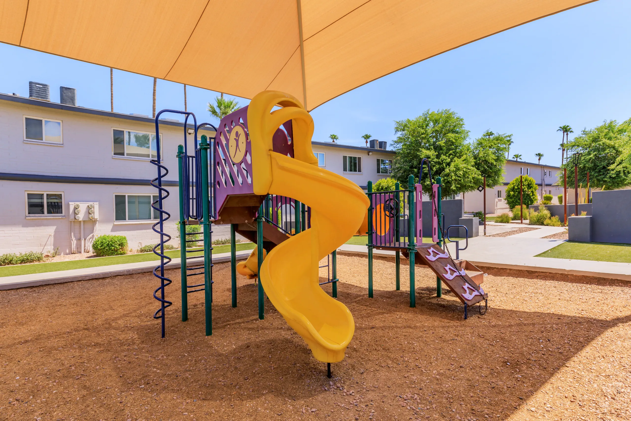 Shaded playground with slide, climbing wall, rubber mulch surface