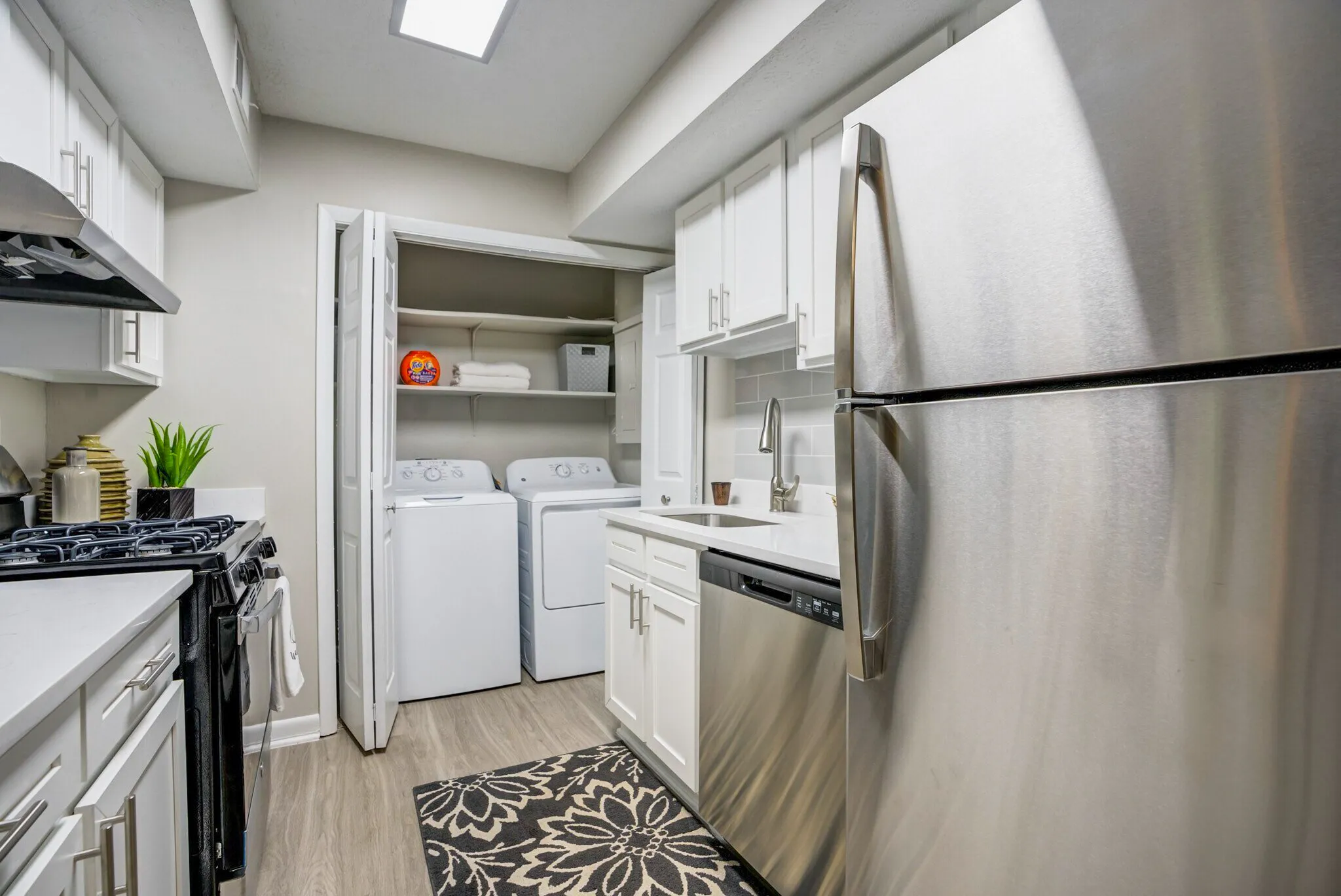 Kitchen with stainless appliances, white cabinetry, quartz countertops, wood-style plank flooring, adjacent laundry closet with washer and dryer