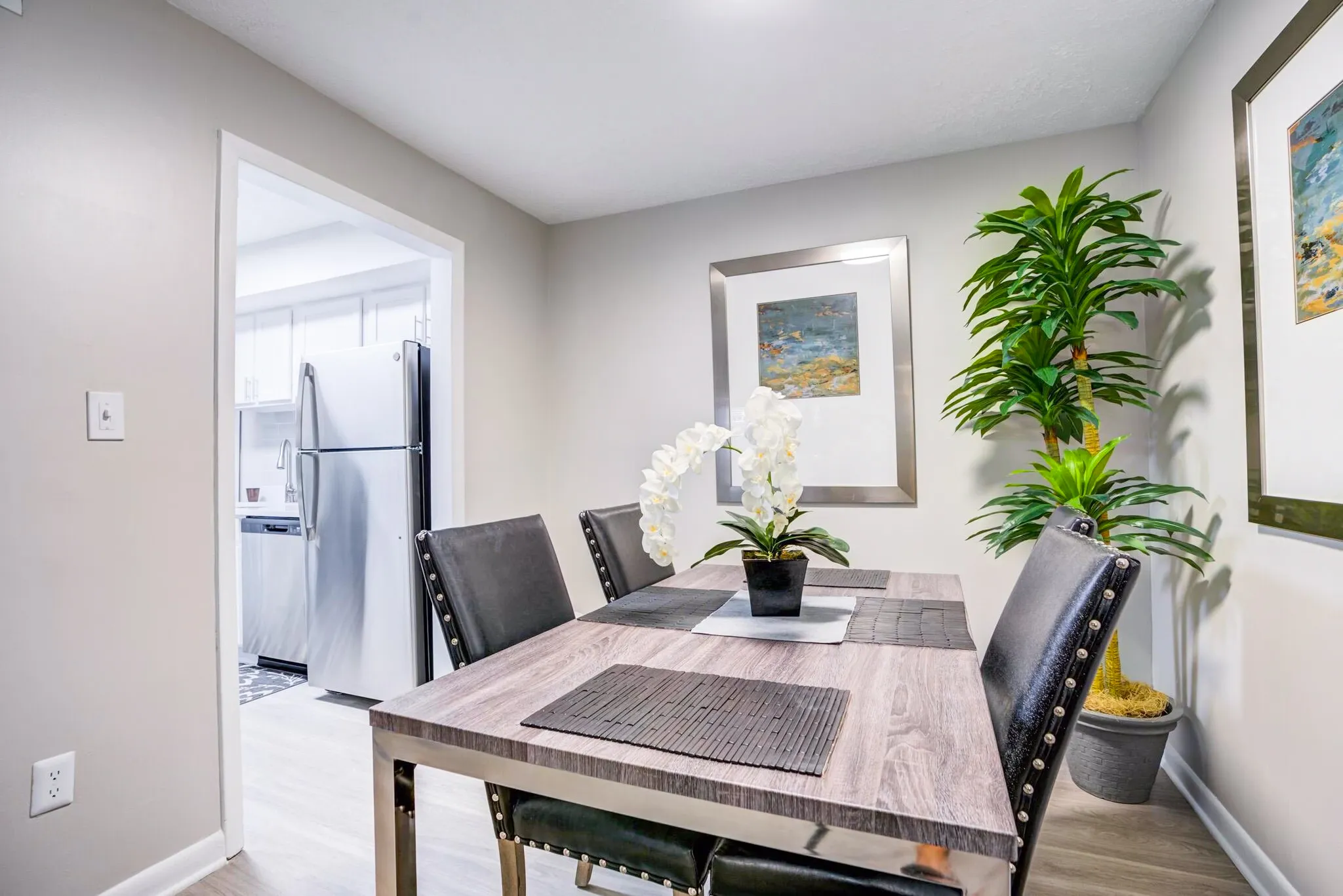 Dining area, wood-style plank flooring, black leather chairs, white orchid centerpiece, kitchenette visible through doorway