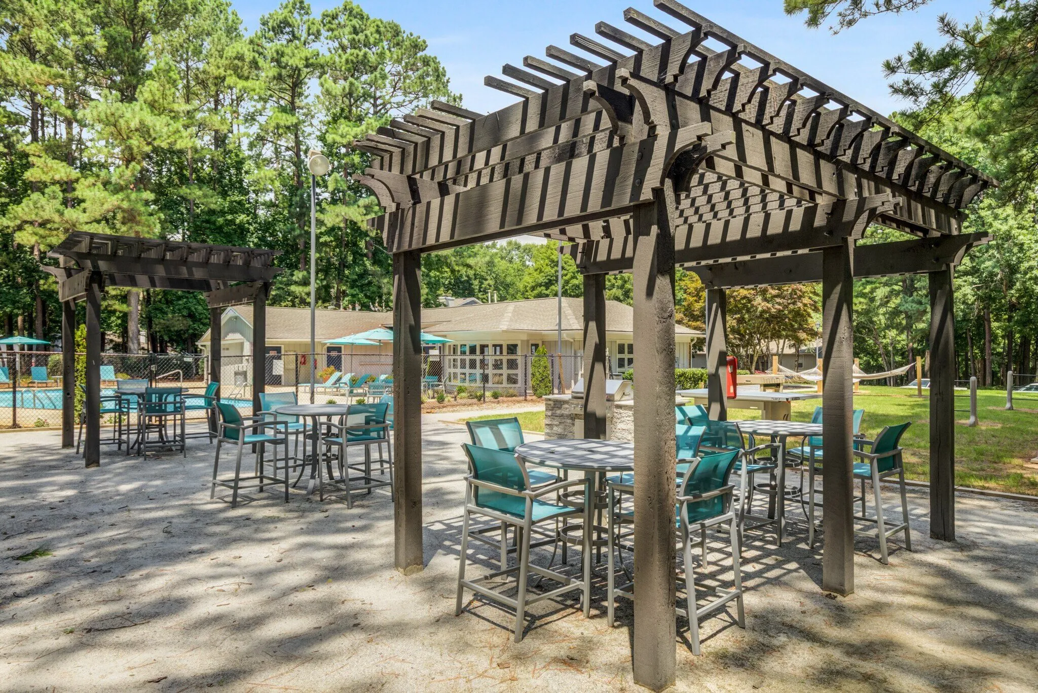 Outdoor pavilion with dark pergola structure, teal bar-height chairs, high-top tables, shade