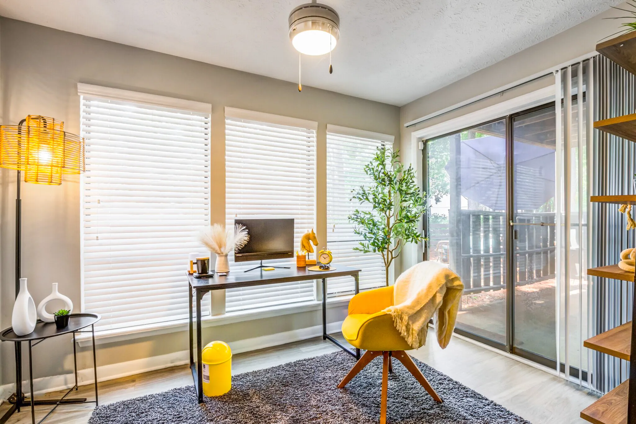 Home office, desk with monitor, yellow accent chair, glass sliding doors, white louvered shutters