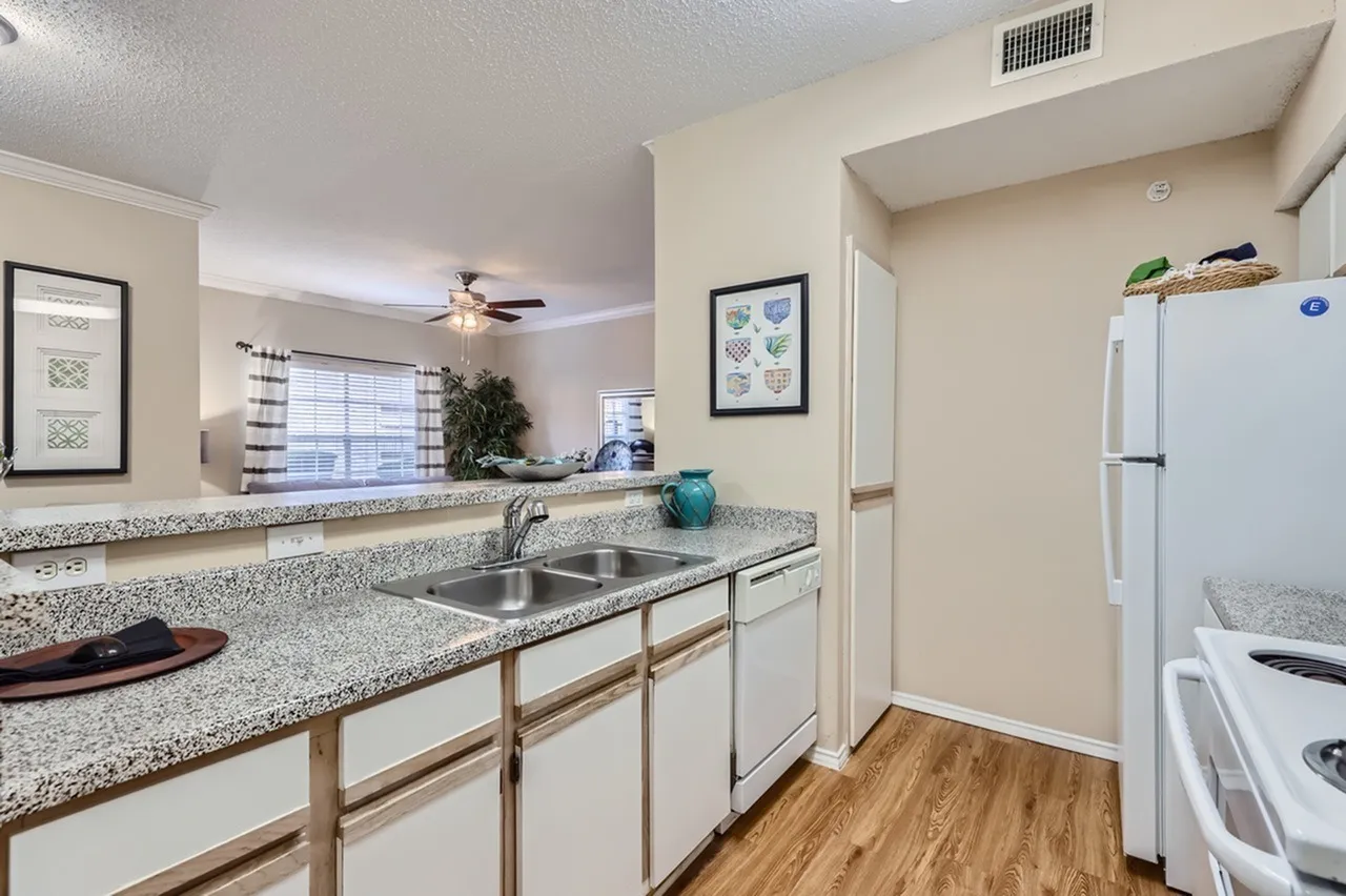 Kitchen sink, speckled countertop, white cabinetry with wood trim, window