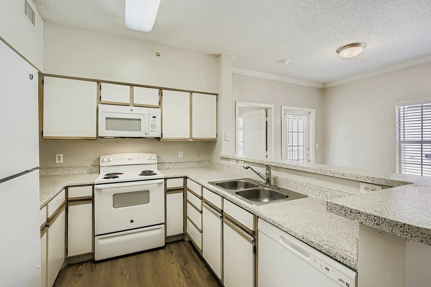 Kitchen, white cabinetry with wood trim, white appliances, speckled countertop