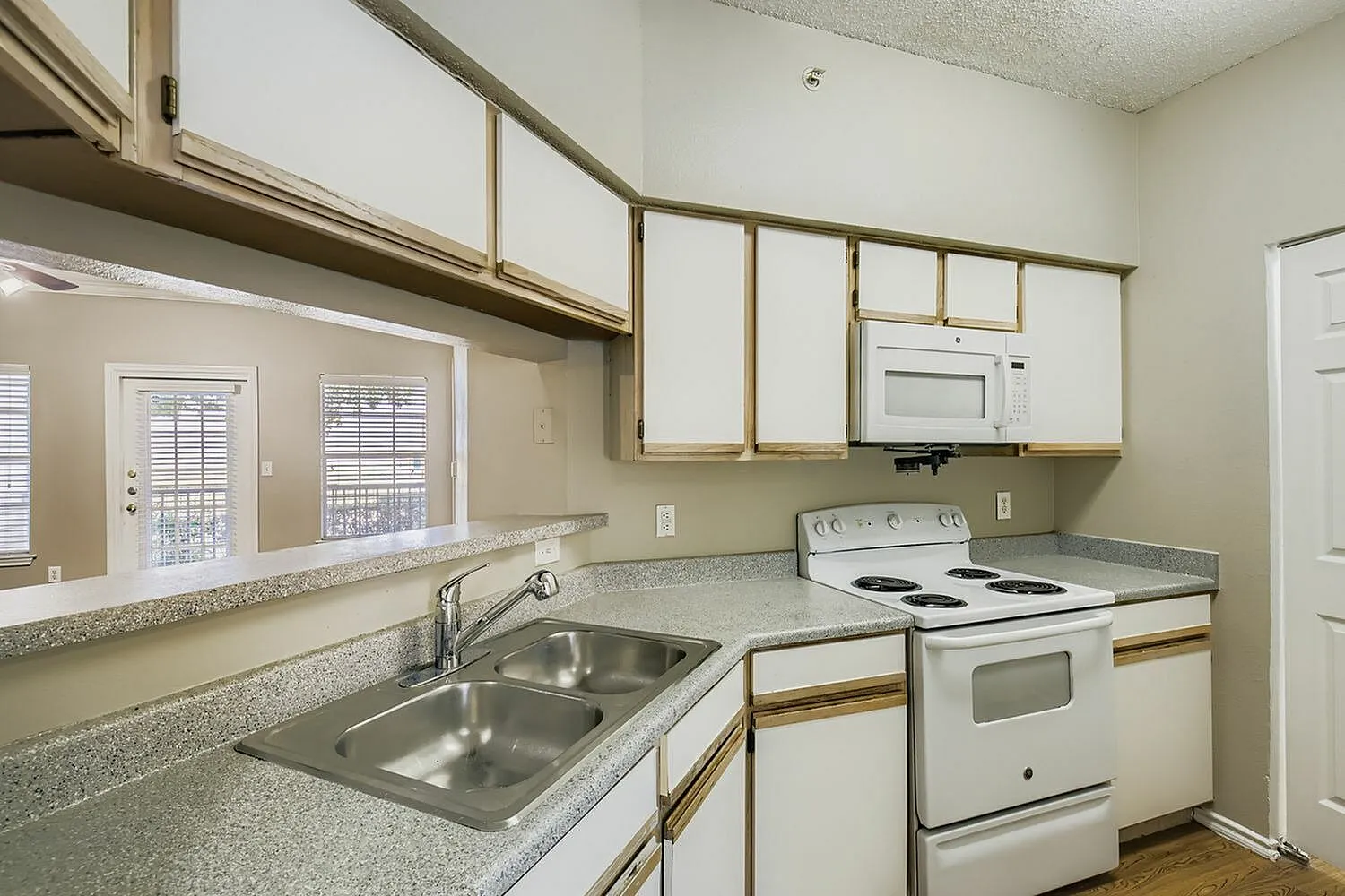 Kitchen, white cabinetry with wood trim, white appliances, speckled countertop
