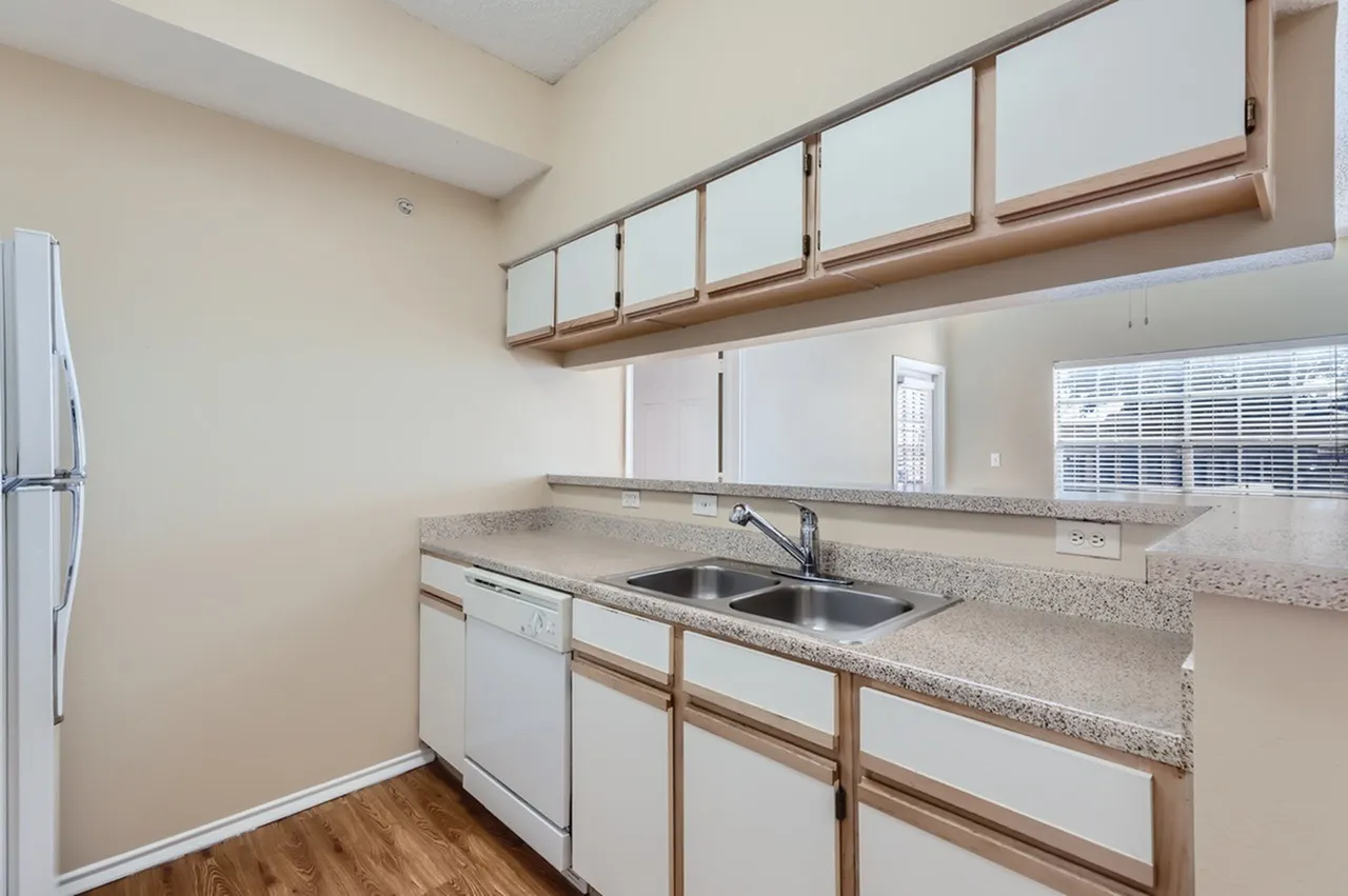 Kitchen sink, speckled countertop, white cabinetry with wood trim