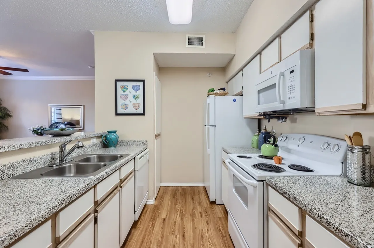 Kitchen, white cabinetry, white appliances, speckled countertop, wood-style plank flooring
