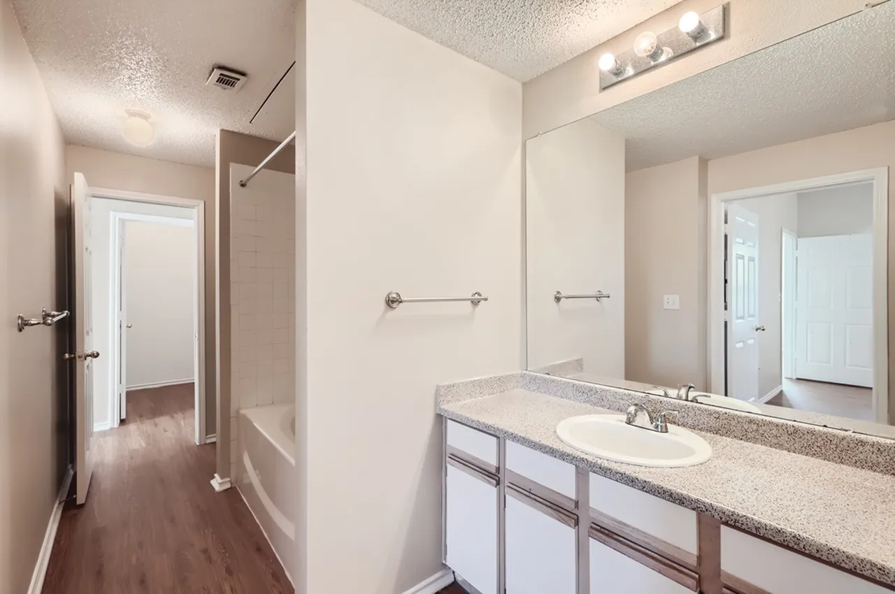 Bathroom vanity, speckled countertop, framed mirror, tub shower