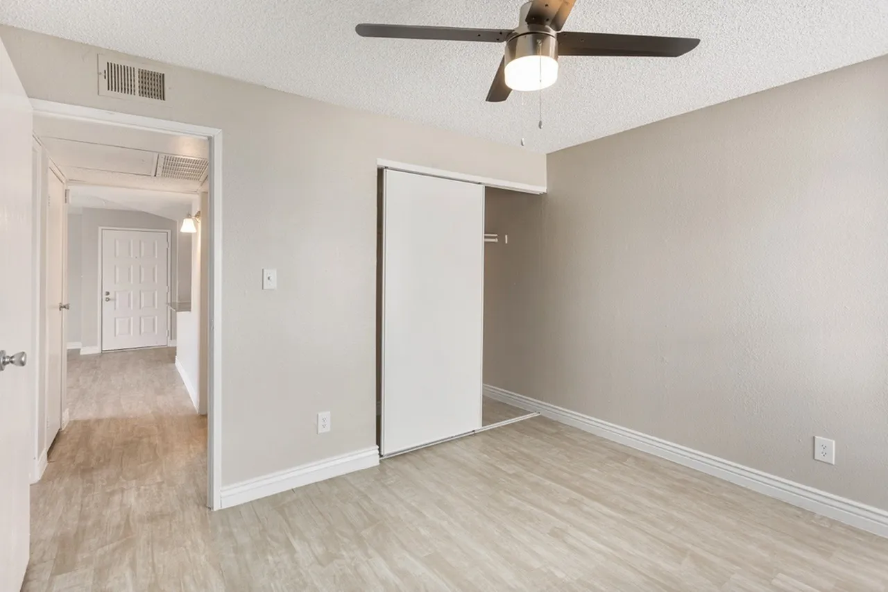Primary bedroom, wood-style plank flooring, ceiling fan with light, white closet doors