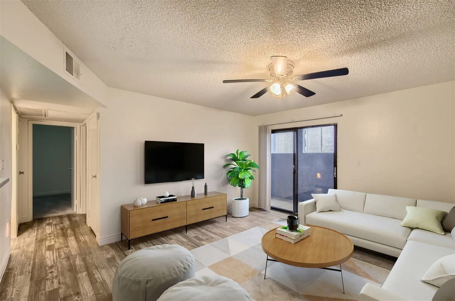 Living room, wood-style plank flooring, ceiling fan, white sofa, mounted TV, wood console table