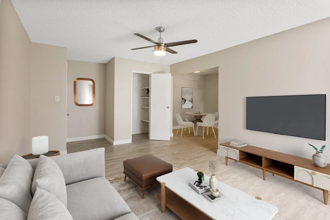 Living room with wood-style plank flooring, ceiling fan, gray sofa, TV mounted on wall, dining area visible through open floor plan