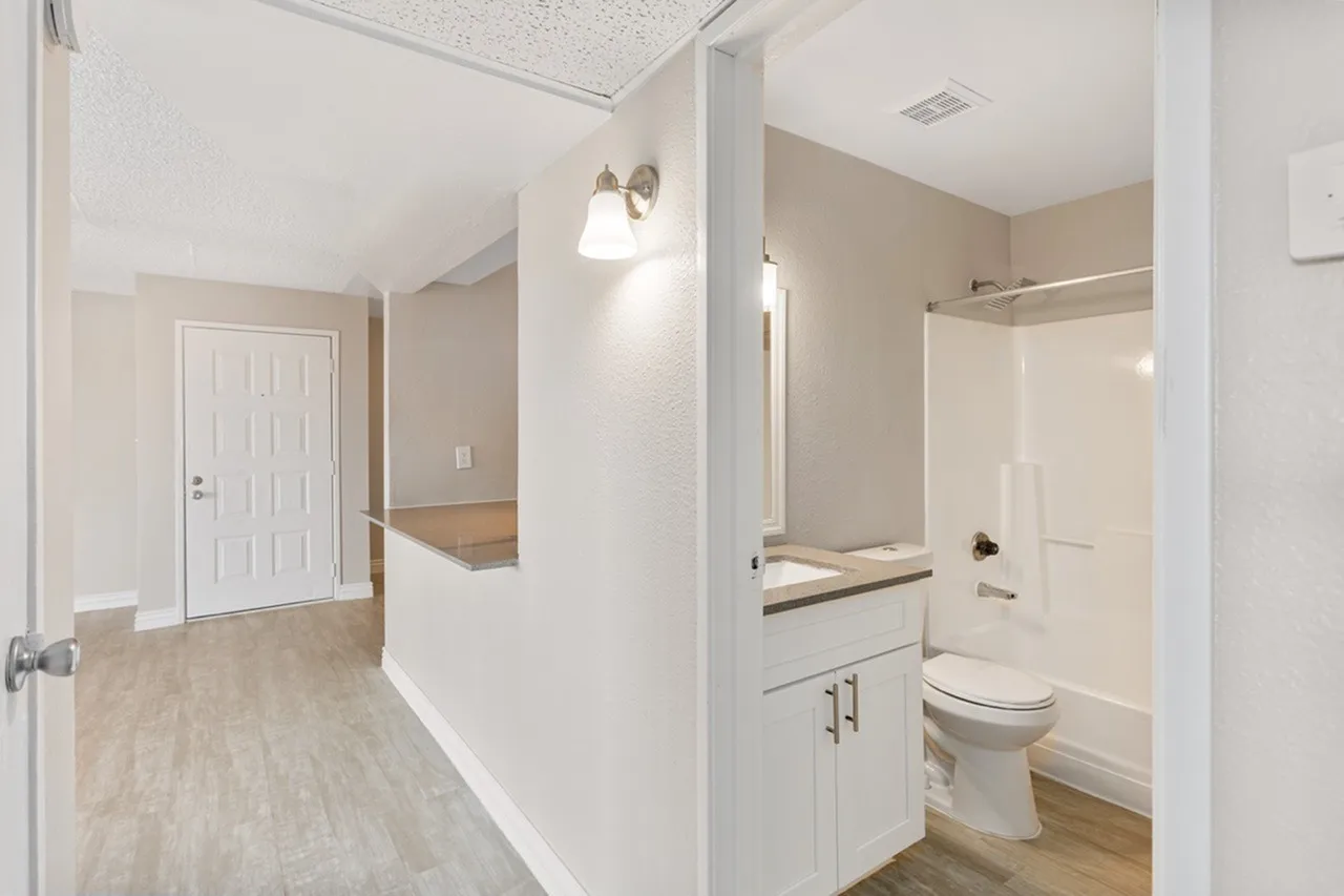 Primary bathroom with white vanity cabinetry, bathroom fixtures, wood-style plank flooring, hallway view