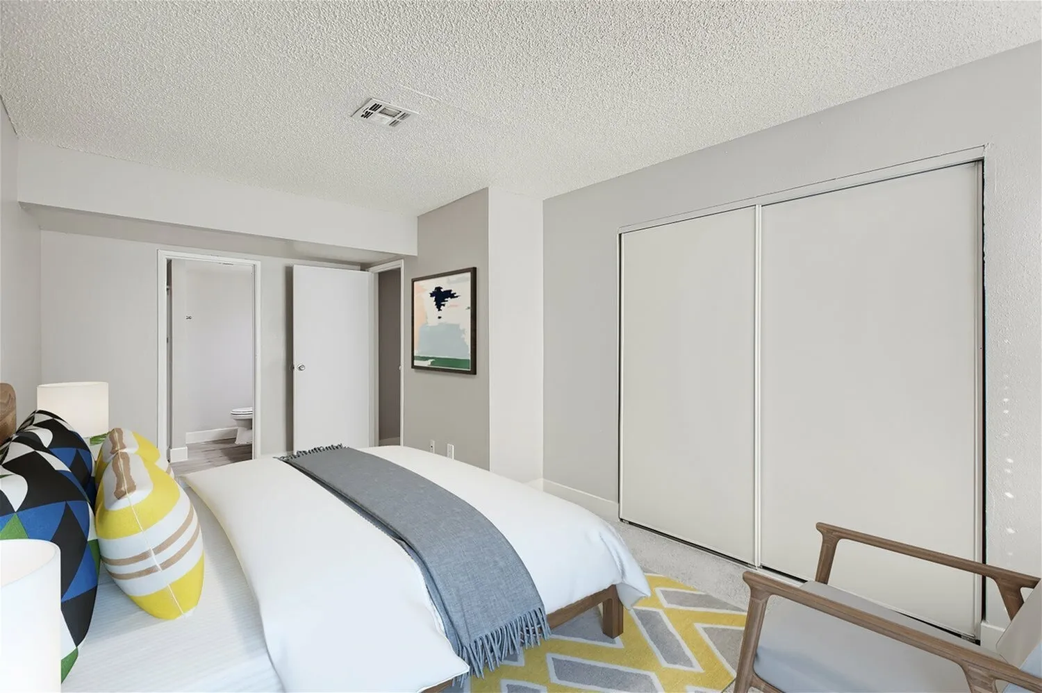 Primary bedroom, bed with blue and white bedding, white closet doors, wood-style plank flooring, geometric yellow rug