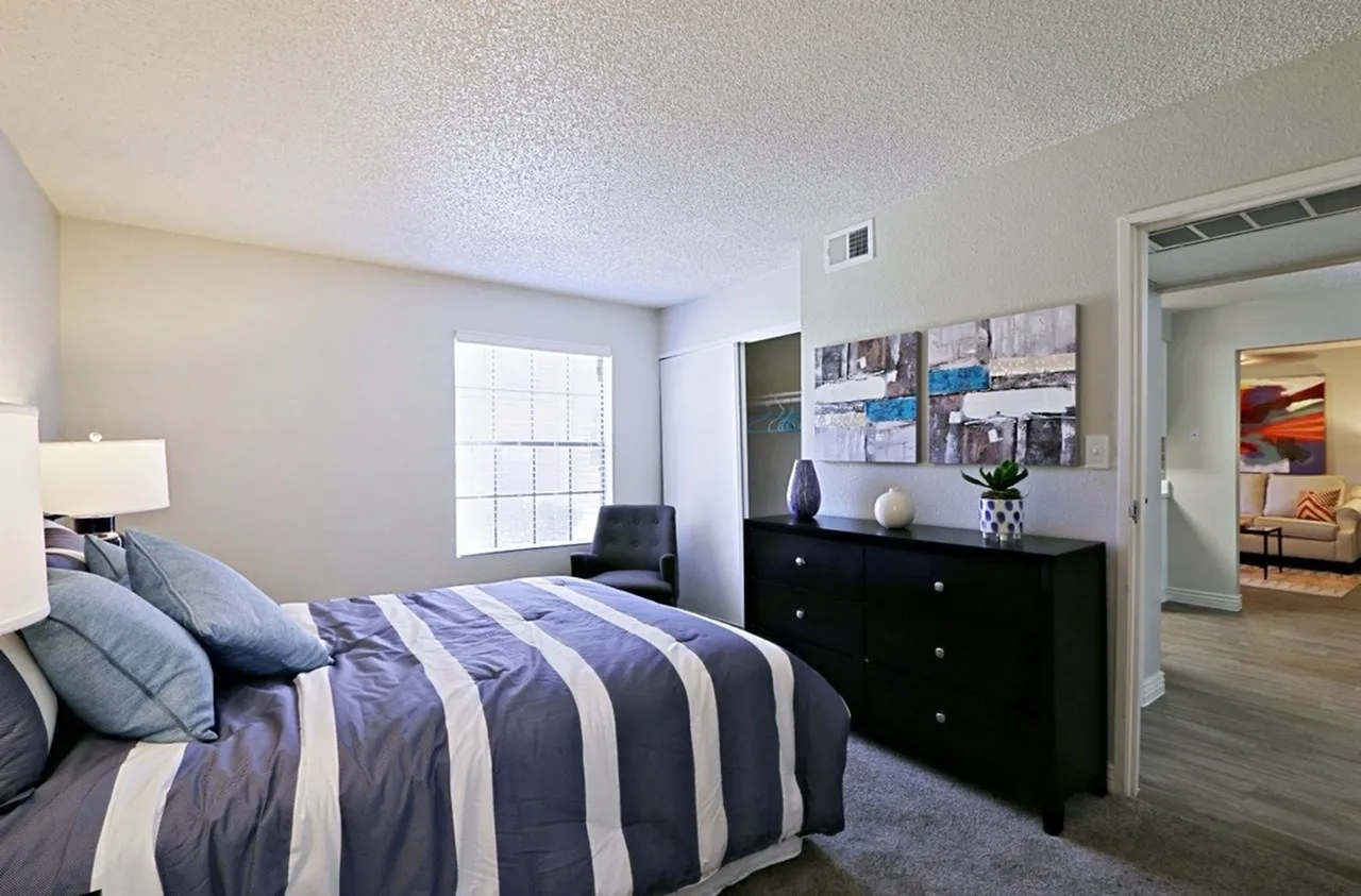 Primary bedroom, striped bedding, black dresser, wood-style plank flooring, window with natural light