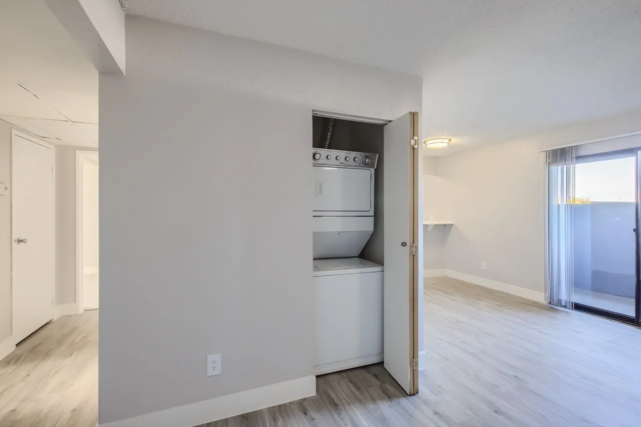 Laundry alcove, stacked washer dryer unit, wood-style plank flooring, open living space