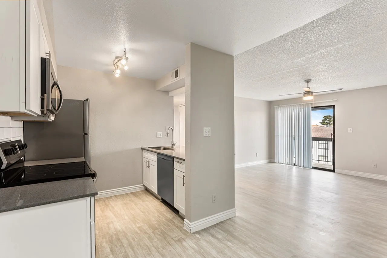 Kitchen with white cabinetry, gray countertops, stainless appliances, wood-style plank flooring, open to living room