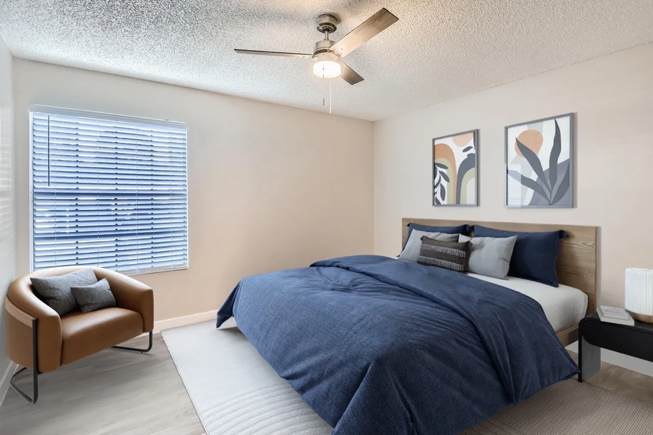 Primary bedroom, blue bedding, wood-style plank flooring, ceiling fan, brown leather chair
