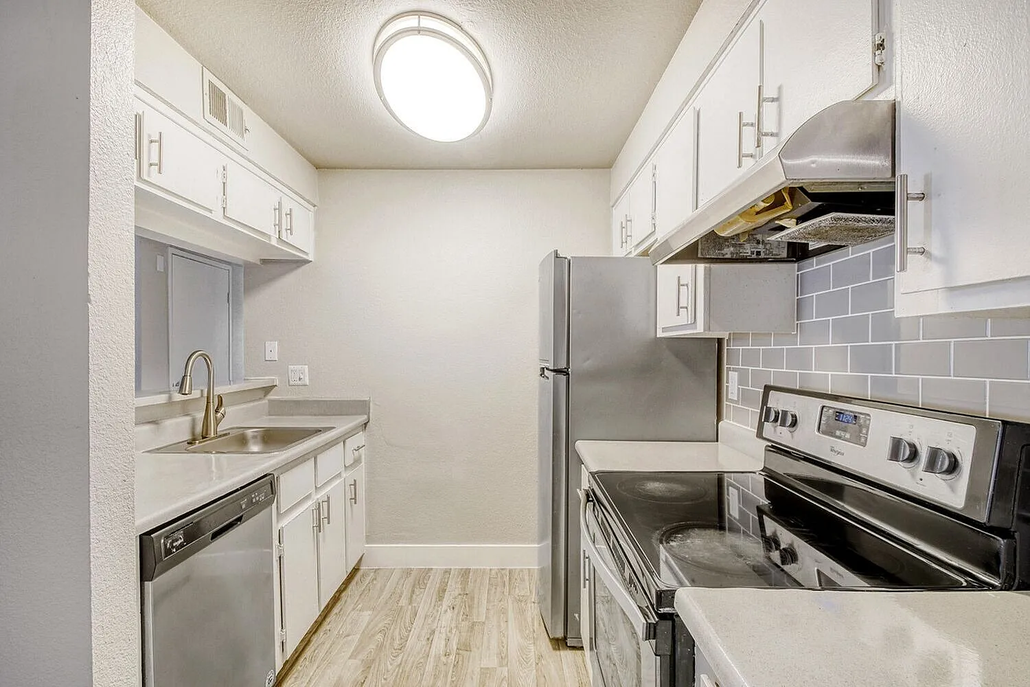 Kitchen, white shaker cabinetry, stainless appliances, gray tile backsplash, wood-style plank flooring